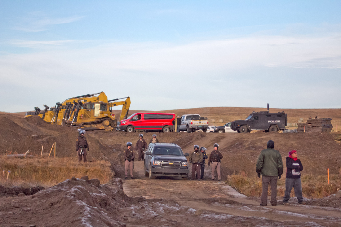 Two Native Americans stand near police guarding construction equipment owned by the DAPL.