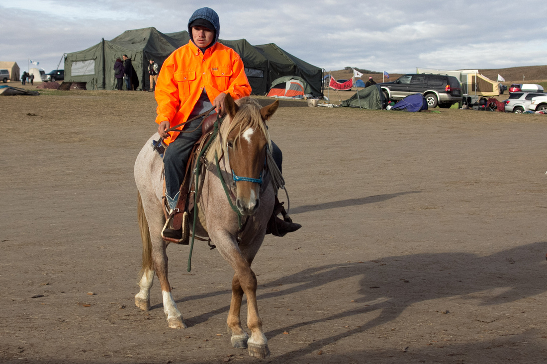 A Native man in a high visibility jacket rides his horse through the campsite at the DAPL Resistance camp in Cannon Ball, ND. Horses are a common sight around the camp and used primary for transportat