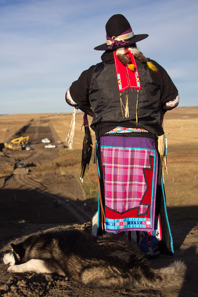 A Native American man and elder that identifies himself as "Dan" stands on a bluff overlooking the DAPL pipeline construction site and sings in his native language.