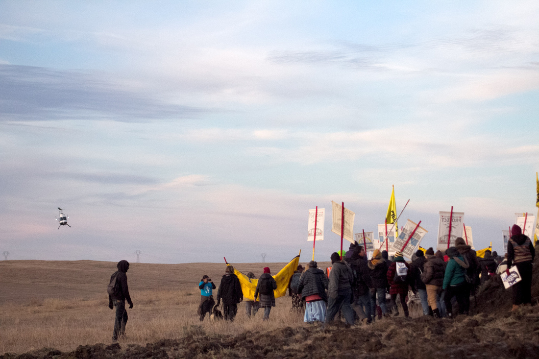 A law enforcement helicopter follows Native American Water Protectors as they walk along the path towards the #DAPL construction site.