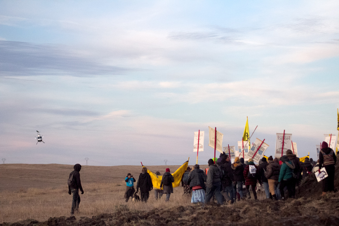 A law enforcement helicopter follows Native American Water Protectors as they walk along the path towards the #DAPL construction site.