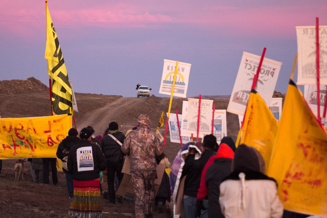 DAPL Resistance Water Protectors march towards a hill under the watchful eyes of law enforcement and private security companies. Behind the hill is the DAPL construction site.
