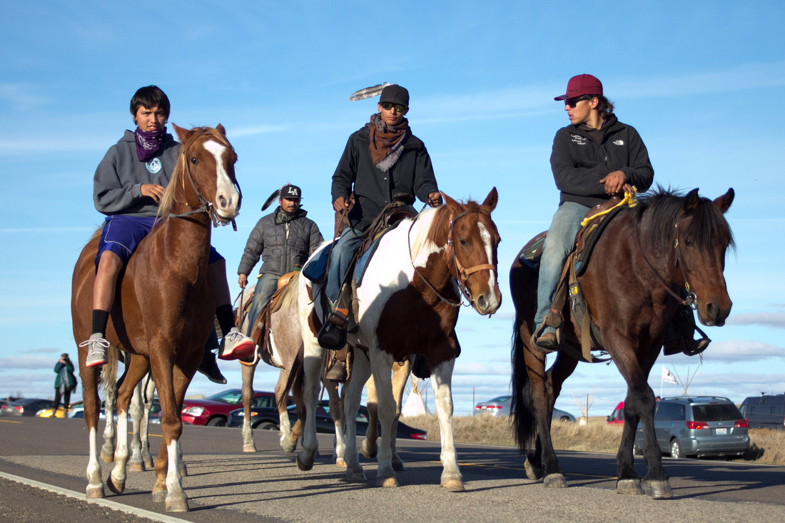 Four Native American men on horseback returning from the front lines near the new location of the DAPL Resistance campsite.